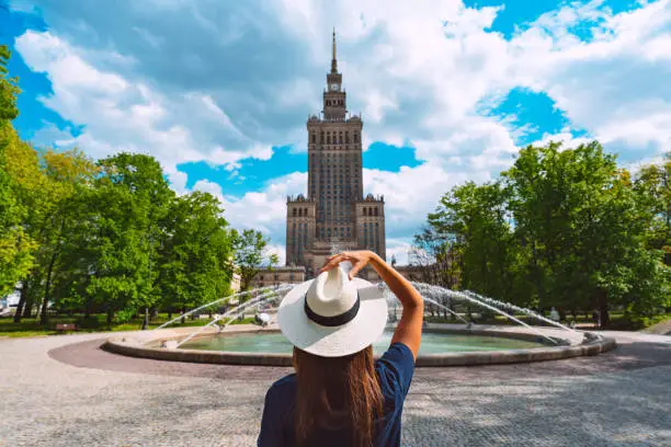 Young tourist woman in white sun hat walking in the park near Palace of Culture and Science in Warsaw city, Poland. Summer vacation in Warsaw. High quality photo