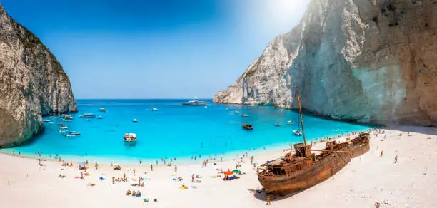 Panoramic view of the famous Navagio shipwreck beach on Zakynthos island, Greece, with people enjoying the light blue colored sea