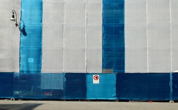 istock Blue and white scaffold plastic sheeting covering a facade under refurbishment, with a no access sign at ground level. 1329827176