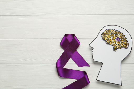 Top view of human head cutout with brain and purple ribbon on white wooden background, space for text. Epilepsy awareness