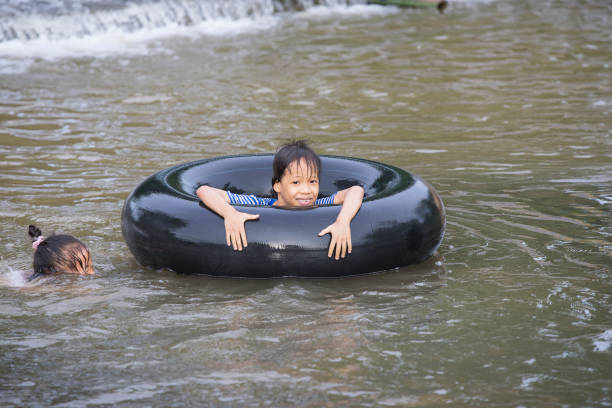 un enfant joue et est resté sur un pneu flottant dans l’eau filmé à chiang mai, en thaïlande. - water sport family inner tube sport photos et images de collection