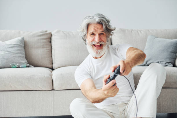 istock Plays video game by using controller. Senior stylish modern man with grey hair and beard indoors 1329832808