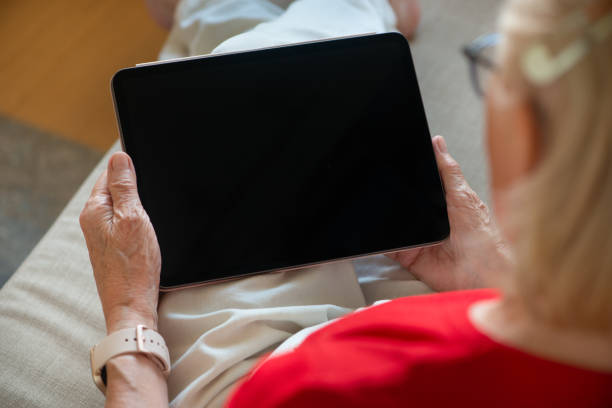 istock Senior woman sitting on sofa and holding blank screen tablet. 1329837530