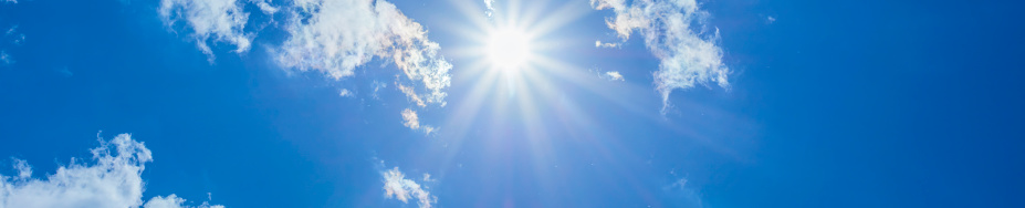 Bright sun with beautiful beams in a blue sky with some light clouds. Space for copy.