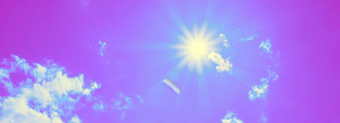 Bright sun with beautiful beams in the sky with some light clouds. Toned in purple color, space for copy.