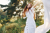 Happy young woman dancing with white cloth in hands outdoors in the forest