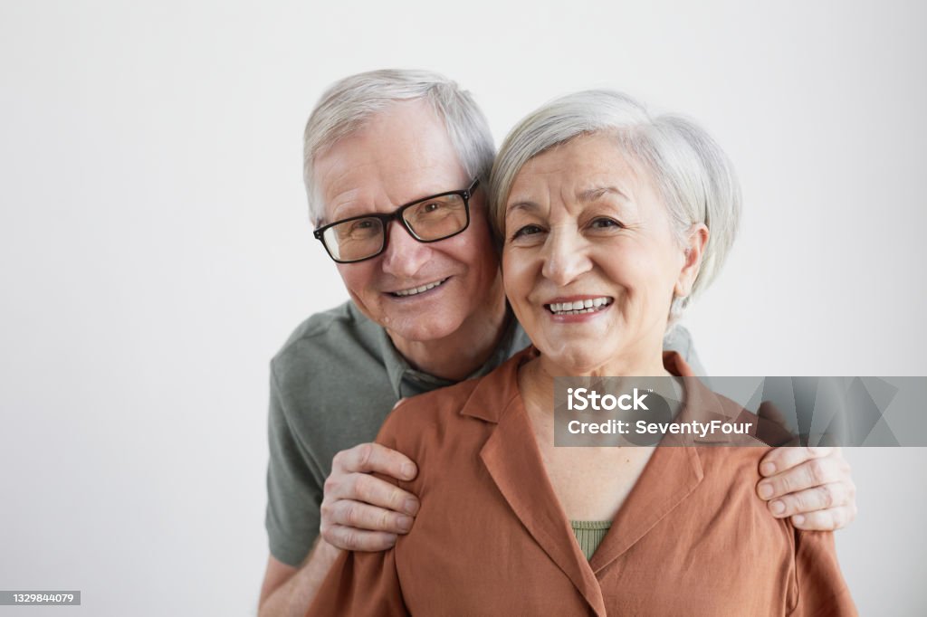 Portrait of Smiling Senior Couple Minimal portrait of happy senior couple embracing husband and looking at camera against white background 80-89 Years Stock Photo