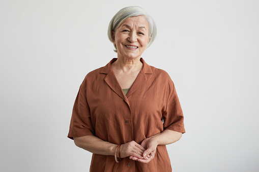 Minimal waist up portrait of modern senior woman smiling at camera while standing against white background