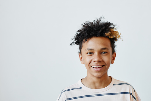 Minimal portrait of mixed-race teenage boy smiling at camera against white background, copy space