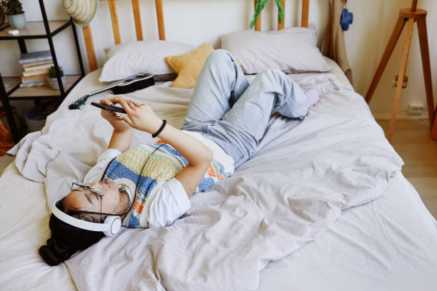 Asian Teenage Girl Laying on Bed High angle view at trendy teenage girl laying on bed and using smartphone in cozy room interior, copy space 13 14 years child teenage girls lying down stock pictures, royalty-free photos & images