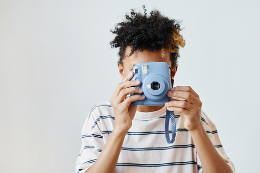 Minimal portrait of mixed-race teenage boy holding instant camera against white background, copy space