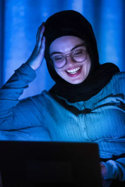 Hijabi Girl at home using laptop to communicate with offshore client