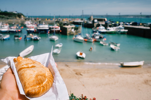 POV of a hand holding a Cornish Pasty above the Harbour at Newquay, Cornwall on a bright sunny June day.