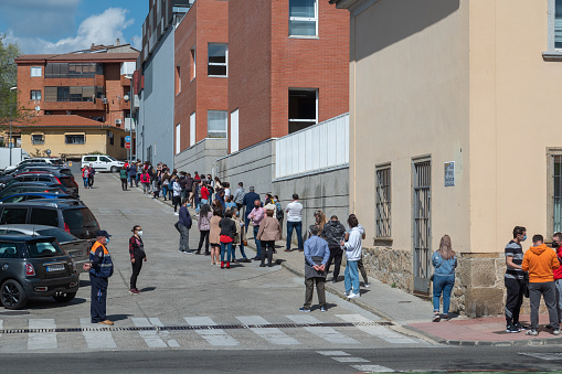 Plasencia, Spain - March 26, 2021: Queue of people with masks and respecting social distance waiting at the door of a medical center to take the free antigen test. Centralized PCR testing.