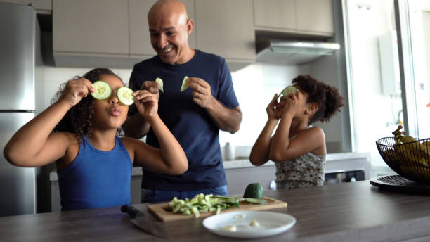 Father and daughters playing in the kitchen with cucumber slices