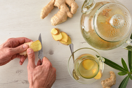 Man preparing ginger infusion on a white table with sliced ginger root and teapot. Top view.