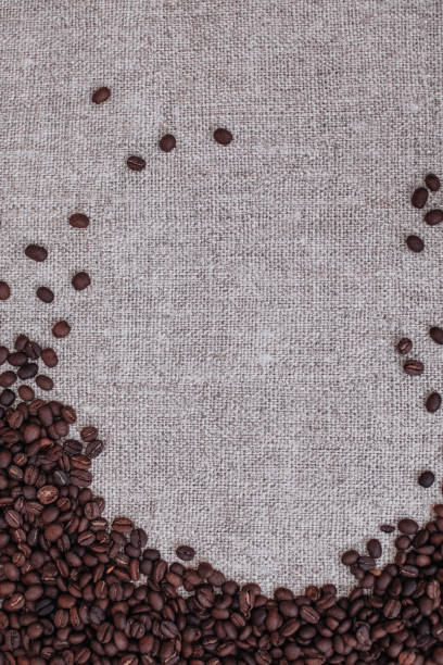 istock Fresh aromatic roasted coffee beans scattered on a beige burlap background. 1329865535