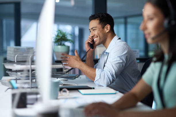 scatto di un giovane che risponde al telefono mentre lavora in un moderno call center - telefono fisso foto e immagini stock