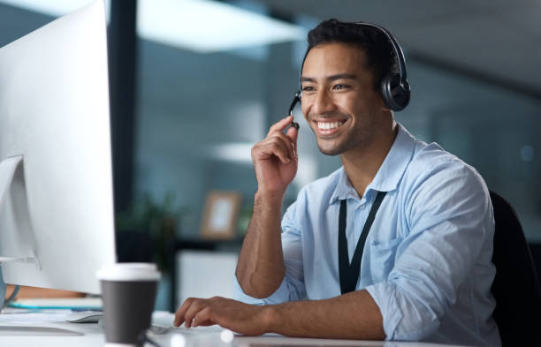 Shot of a young man using a headset and computer in a modern office Have you heard about our latest package? customer service representative photos stock pictures, royalty-free photos & images