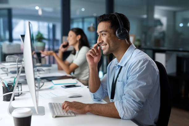 foto de un joven usando un auricular y una computadora en una oficina moderna - it support fotografías e imágenes de stock