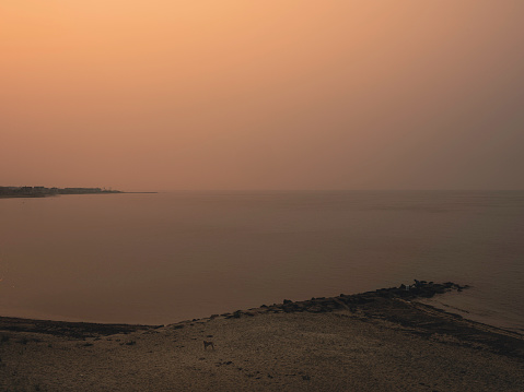 Summer seascape on Cape Cod on hazy morning at sunrise with soft fog and red sun illuminating through the thick darker than usual  air