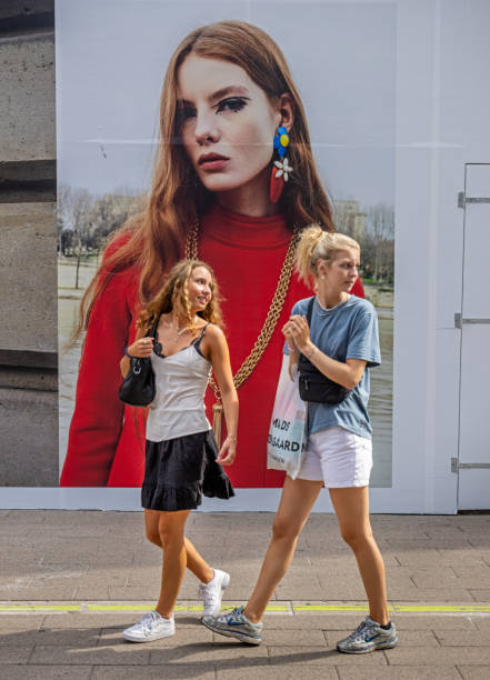 Two beautiful teenage girls passing a poster for couture in the center of Copenhagen