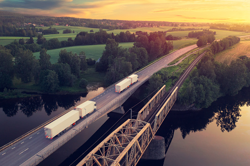 Two trucks with trailers on the road at sunset through a rural landscape in the Dalarna region of Sweden.