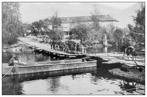 Antique black and white photograph of people from islands in the Caribbean and in the Pacific Ocean; Cuba, Hawaii, Philippines and others: American ammunition wagon crossing a stream on a pontoon bridge, Philippines
