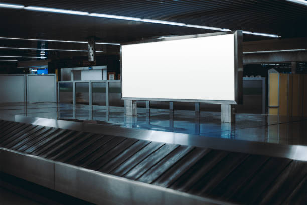 Billboard mockup, baggage claim area View of a baggage claim area in a hall of a modern airport arrival zone with luggage conveyor belt, with a selective focus on a template of a blank advertising poster or an information billboard carousel photos stock pictures, royalty-free photos & images