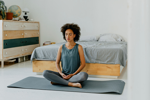 Mindfulness concept: pretty mixed race woman meditating on her bedroom floor