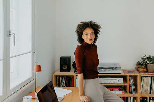 A young professional woman leaning on her desk while looking at camera