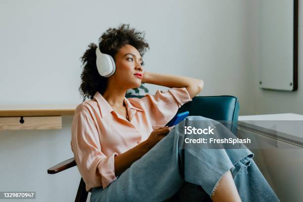 Relaxed Young Woman With Headphones On Sitting In An Armchair And Listening To Her Favorite Podcast Stock Photo - Download Image Now