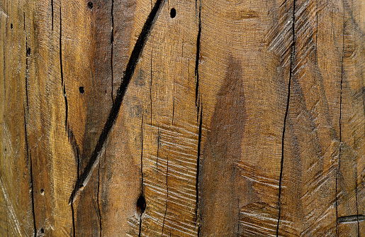 Weathered and scratched rustic wooden board.High angle view of a flat textured wooden board backgrounds. It has a beautiful nature and abstractive pattern. A close-up studio shooting shows details and lots of wood grain on the wood table. The piece of wood at the surface of the table also appears rich wooden material on it. The wood is dark brown color with darker brown lines and pattern on the bottom. Flat lay style. Its high-resolution textured quality.The close-up gives a direct view on the table, showing cracks and knotholes in the wood.