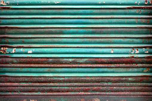 old rusty metal door gate of a garage painted in turquoise blue color and oxidated in red, orange and brown tones - weathered steampunk background with horizontal lines