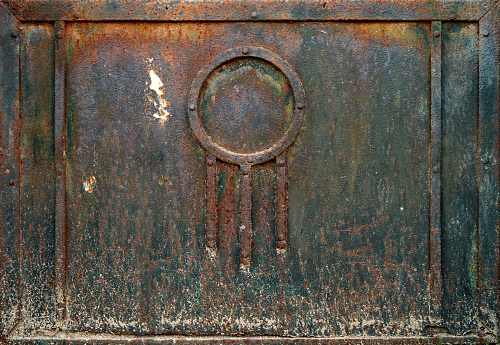 rusty ornate door of an industrial black metal box - worn steam punk dark surface with dirty and weathered background