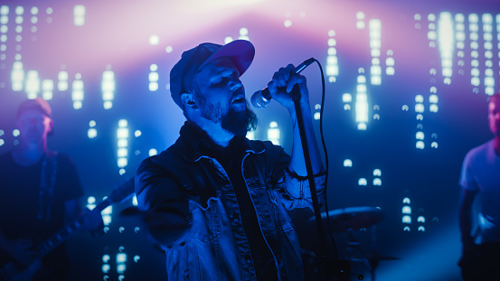 Rock Band Performing at a Concert in a Night Club. Portrait of a Lead Singer Singing into Microphone. Live Music Party in Front of Bright Colorful Strobing Lights on Stage.