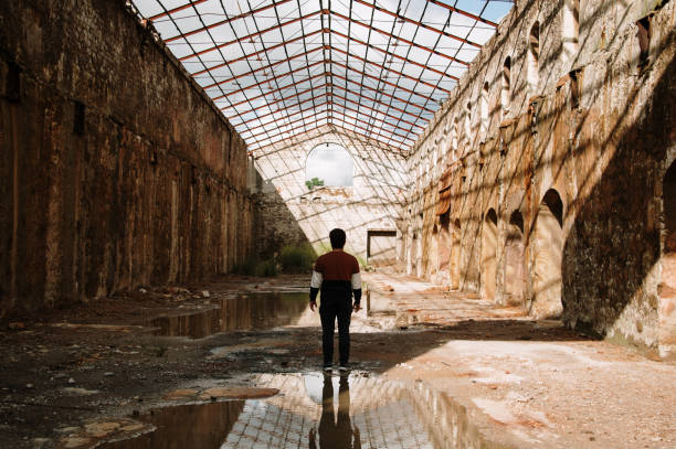 Young man inside an abandoned building Silhouette of a young man and reflection inside an abandoned industrial building abandoned place stock pictures, royalty-free photos & images