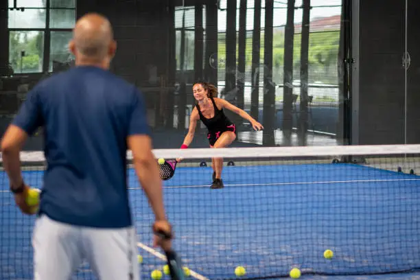 Monitor teaching padel class to woman, his student - Trainer teaches young girl how to play padel on indoor tennis court