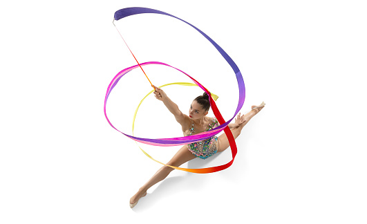 Young graceful girl, female rhythmic gymnast training with bright colored ribbon sitting in a twine isolated over white studio background. Copyspace for ad