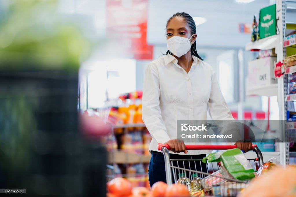 Woman shopping in supermarket wearing coronavirus face mask. N95 Face Mask Stock Photo