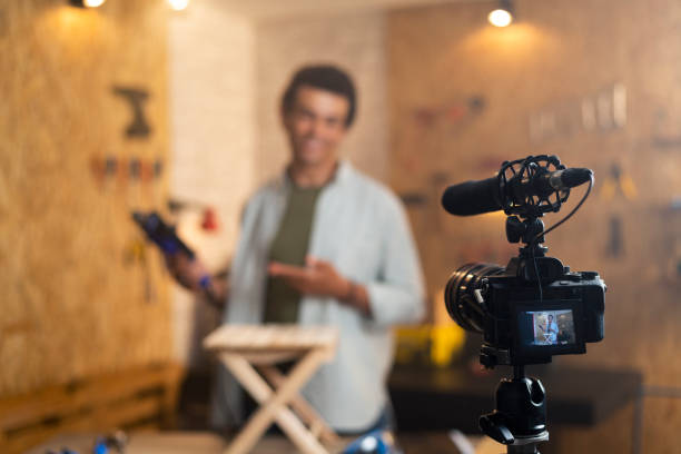 istock DIY carpenter filming a blog about drill with focus on camera and a carpenter blurred in the back 1329881026