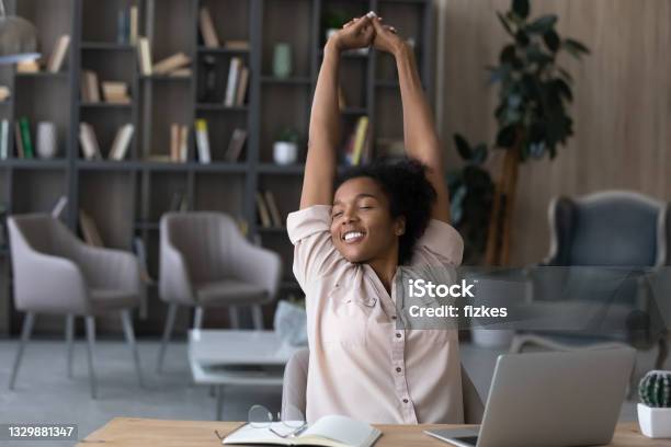 Happy carefree African American woman stretching hands at workplace