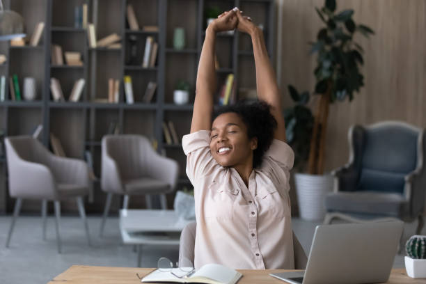 Happy carefree African American woman stretching hands at workplace Happy carefree African American woman stretching hands at workplace, leaning back in comfortable chair, student or freelancer relaxing enjoying break after work done, sitting at desk with laptop smooth stock pictures, royalty-free photos & images