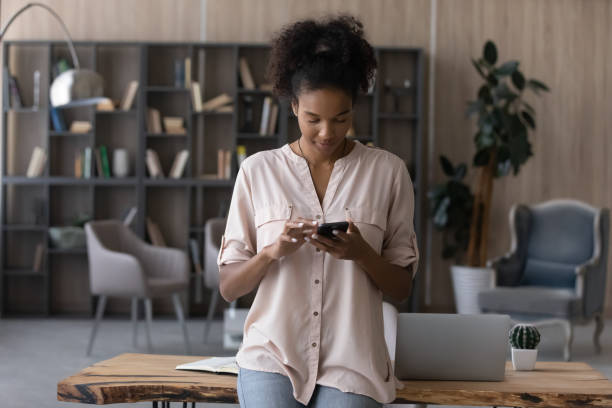 istock Confident African American woman using smartphone, standing near work desk 1329881369