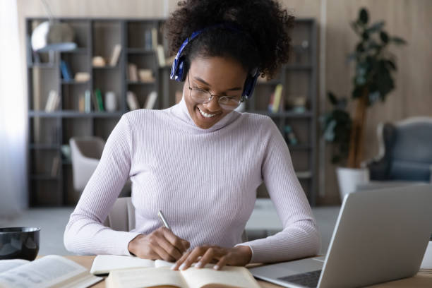 istock Smiling African American woman in headphones taking notes, using laptop 1329881377