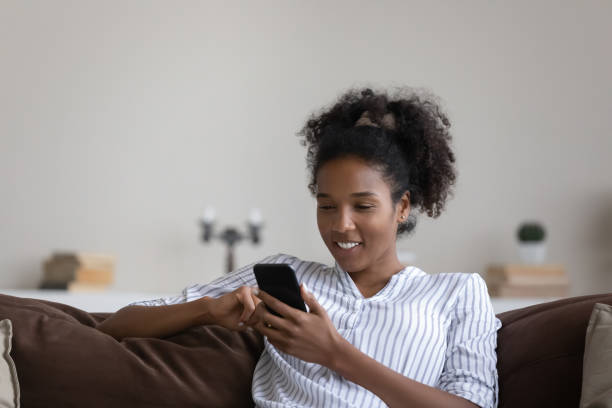 istock Smiling African American young woman using smartphone, sitting on couch 1329881390