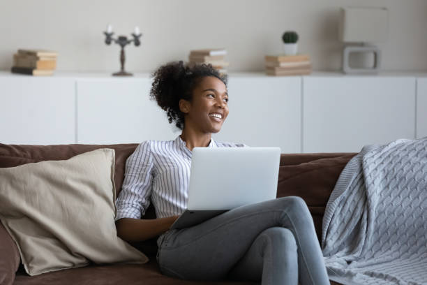 Smiling dreamy African American young woman distracted from laptop