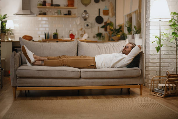istock Tired man laying on sofa and falling asleep late at night 1329883261