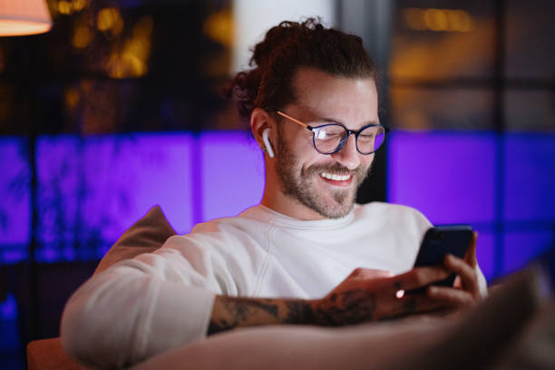 мужчина пишет сообщения по мобильному телефону, отдыхая дома поздно ночью - internet dating audio стоковые фото и изображения