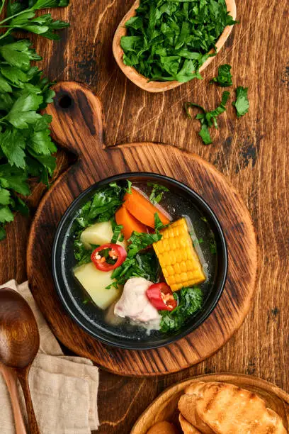 Photo of Chilean meat soup with pampkin, corn, fresh coriander and potatoes on old wooden table background. Cazuela. Latinamerican food.